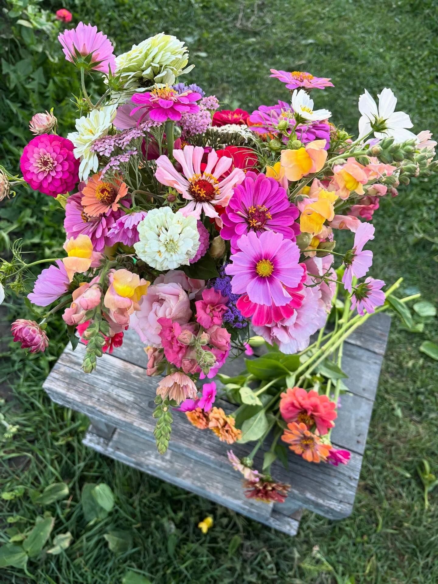 A loose, late-summer bouquet of zinnias, cosmos, and dahlias on a weathered wooden crate in the garden.